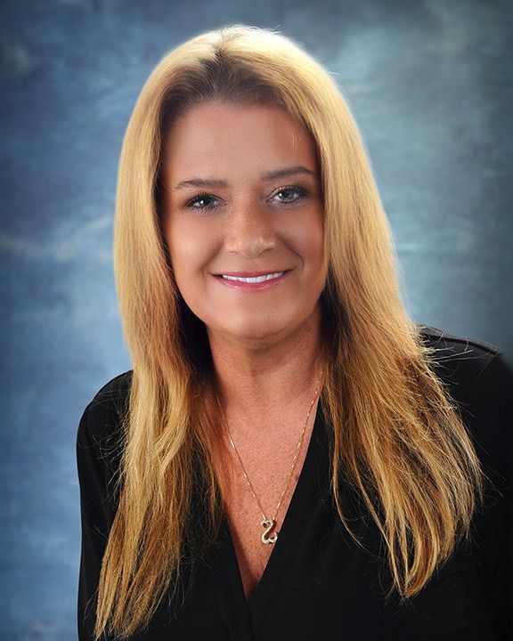 A woman with long blonde hair is wearing a black shirt and a necklace.