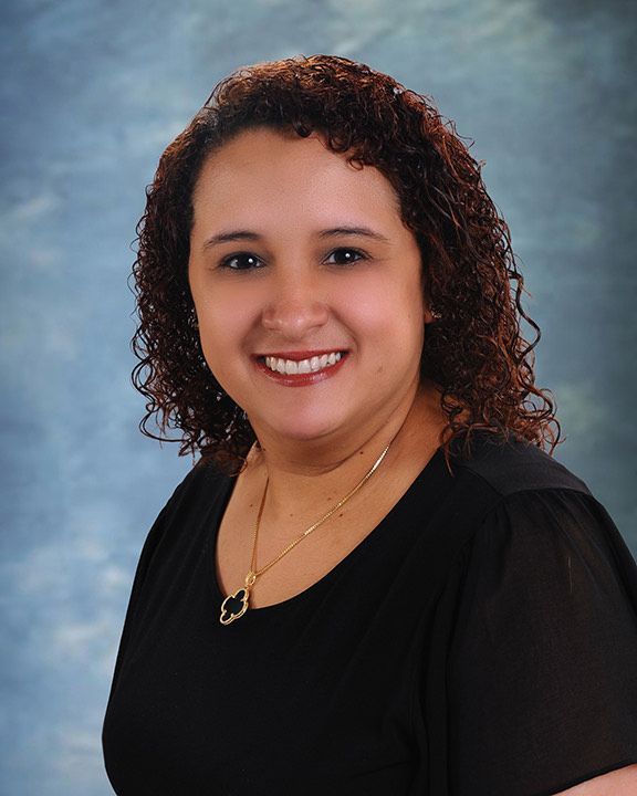 A woman with curly hair is wearing a black shirt and a gold necklace